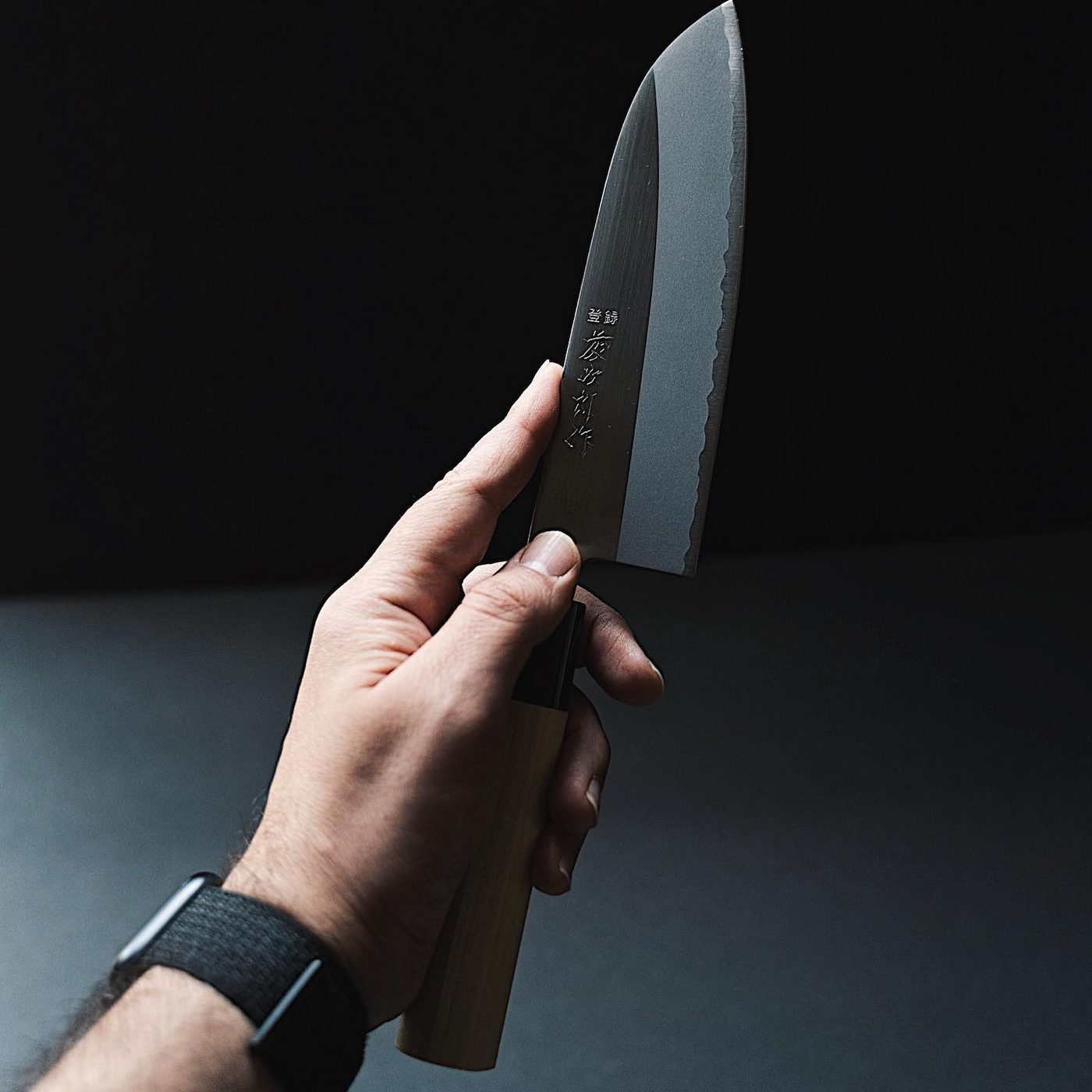 Hand holding Japanese santoku knife, dark moody